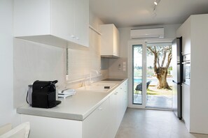 Eine moderne Küche mit weißen Schränken, einem eingebauten Ofen und Blick ins Freie durch eine Glastür.