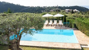Ein Swimmingpool mit Liegestühlen und Sonnenschirmen, umgeben von Grünflächen und Hügeln.