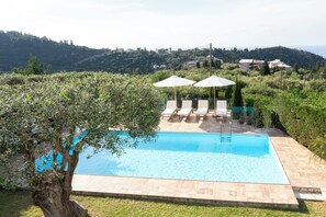 Ein Swimmingpool mit Liegestühlen und Sonnenschirmen, umgeben von Grünflächen und Hügeln.