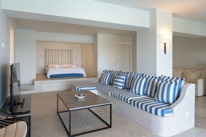 Ein modernes Wohnzimmer mit einem Ecksofa, einem Flachbildfernseher, einem Couchtisch und einem Bett mit Streifenmuster an der Kopfteil.