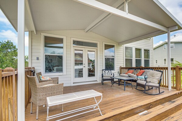 A covered porch with wicker furniture, a white metal bench, and a rocking chair.