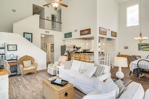 A spacious living area with a white sofa, wicker chair, and dining table with chairs. A staircase leads to an upper level. - Bayou Breeze! Waterfront Home w/ Dock + Deck (Pass Christian)