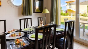 Uma área de refeições com uma mesa posta para quatro pessoas, uma janela com cortinas e vista para um edifício.