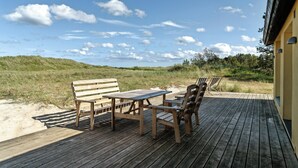 A wooden deck with a table and chairs, overlooking a beach with dunes and a clear sky. - Stone house's simplicity in Jerup's vicinity (Jerup)