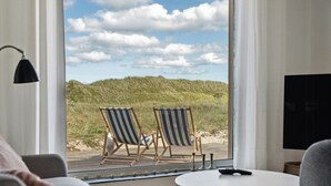 A room with a large window, two beach chairs, a small table, and a lamp. - Stone house's simplicity in Jerup's vicinity (Jerup)