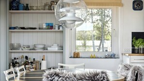 A kitchen with white cabinetry, a dining table with chairs, a hanging light fixture, and a window with a view of trees. - Stone house's simplicity in Jerup's vicinity (Jerup)