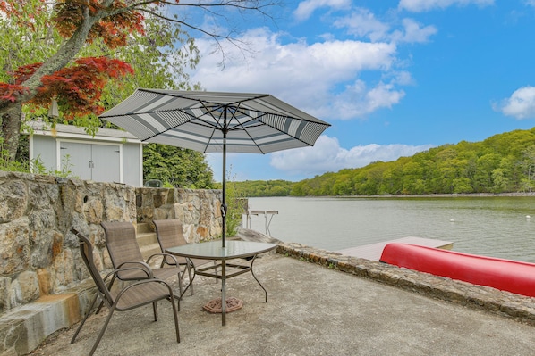 A patio with a table and chairs, an umbrella, and a view of a lake.