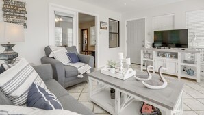 A living room with a grey sofa, a coffee table with decorative swans, a television, and a white cabinet.