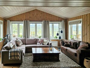 Ein gemütliches Wohnzimmer mit Holzbalkendecke, großen Fenstern, einem Teleskop und einem Kamin.