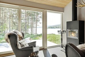 A modern living room with a fireplace, large windows, and a view of a forest and lake. - Historic cabin idyll by Espedalsvannet (Espedalen)