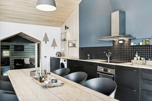 A modern kitchen with a wooden dining table, black chairs, a built-in oven, and a black tiled backsplash. - Historic cabin idyll by Espedalsvannet (Espedalen)