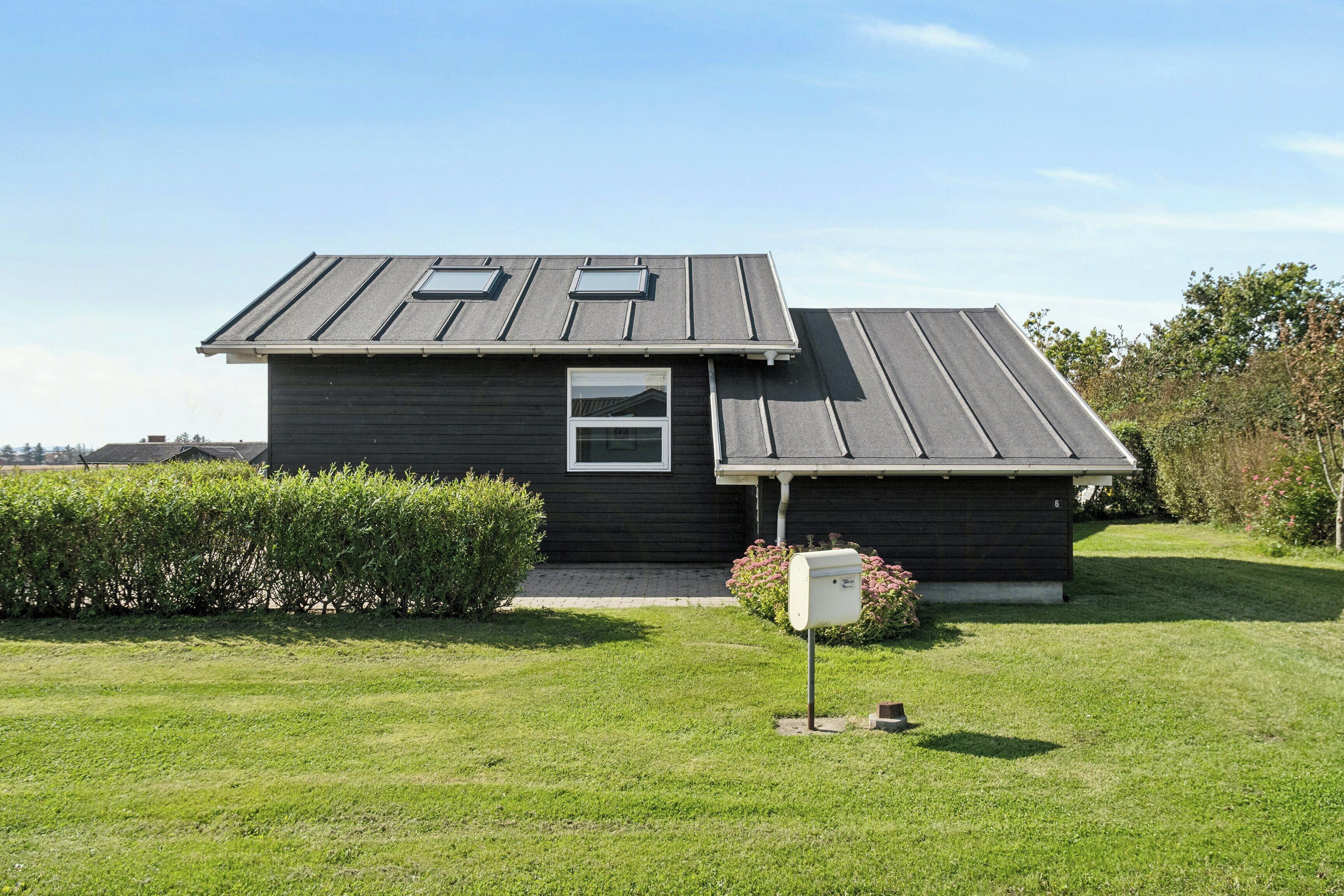 A single-story house with a dark exterior, a small window, and a mailbox in the front yard.