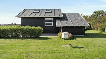 A single-story house with a dark exterior, a small window, and a mailbox in the front yard.