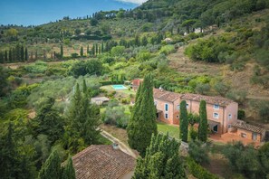 Eine Villa an einem Hang mit Swimmingpool, umgeben von üppiger Vegetation und hoch aufragenden Zypressen.