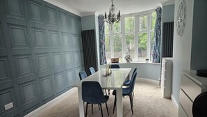 A dining area with a white table, blue chairs, a chandelier, and a view through large windows. - Tranquil Hope Valley Retreat With 3 Bedrooms (Hope Valley)