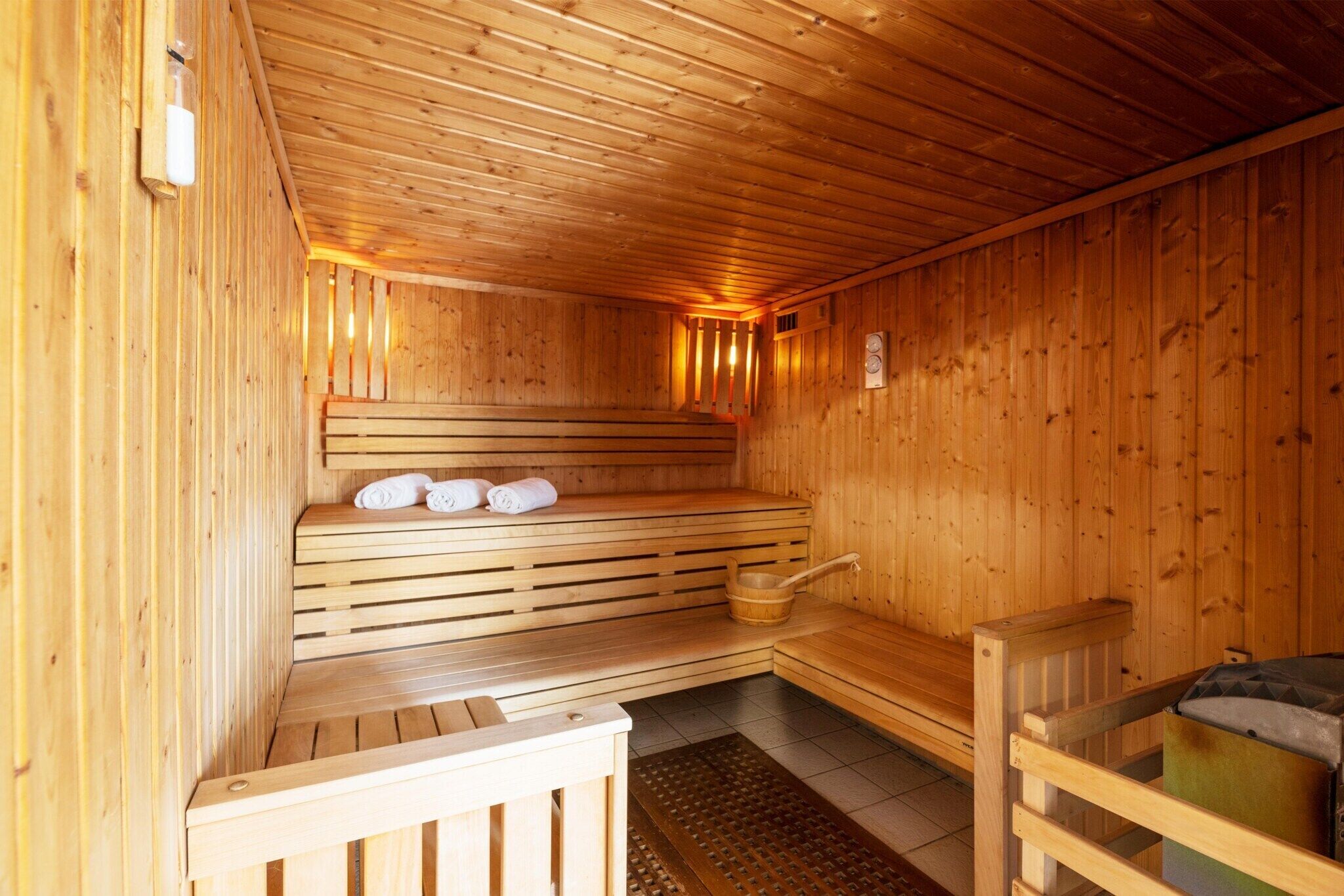 Una sauna de madera con bancos, un banco con toallas y un balde de madera.