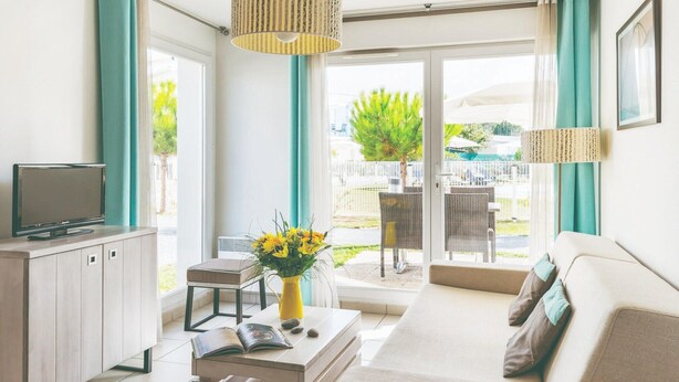 Una sala moderna con sofá, televisor, mesa de comedor y balcón con mobiliario exterior.