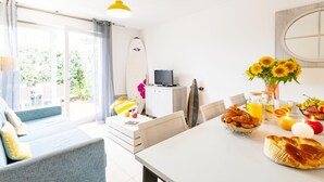 Una habitación luminosa con sofá, mesa de desayuno, una tabla de surf y televisor.