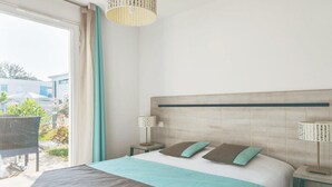 Habitación de hotel con cama, una silla, mesita de noche, lámpara y vista al exterior.