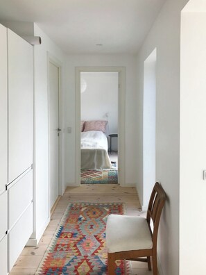 A narrow hallway leading to a bedroom with a bed, a chair, and a colorful rug. - Modern house in Munkerup near Gilleleje (Gilleleje)