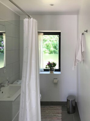 A bathroom with a bathtub, a window with a view of greenery, a toilet, and a trash can. - Modern house in Munkerup near Gilleleje (Gilleleje)