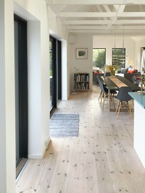 Ein moderner Essbereich mit Holzboden, einem Esstisch mit Stühlen, einem Bücherregal und Blick durch eine Glastür.