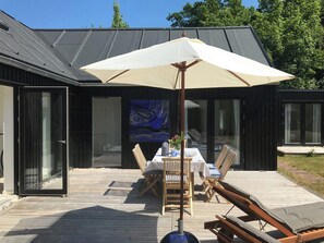 Ein moderner Essbereich im Freien mit Tisch, Stühlen und einem großen Sonnenschirm.