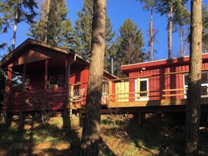 Zwei rote Holzhütten mit Holzbalkonen, umgeben von Bäumen.