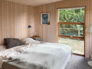 Ein Schlafzimmer mit großem Fenster, Holzwänden, einem Bett mit Kissen, einem Nachttisch und einer Lampe.
