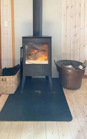 Ein Kaminofen mit Feuer, ein Logkorb und ein gewebter Korb auf dem Boden.
