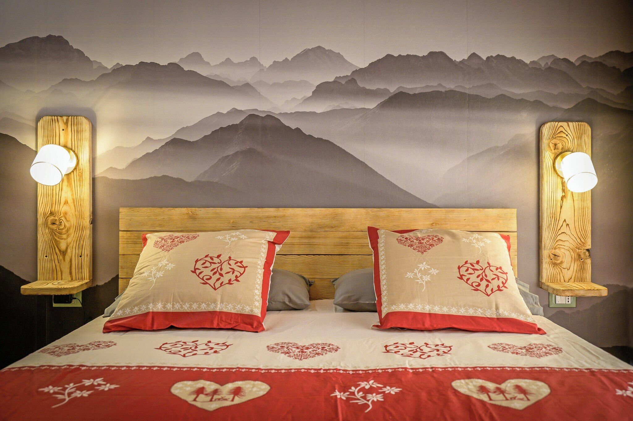 Un lit avec une tête de lit en bois, deux lampes de chevet et une fresque murale représentant des montagnes.