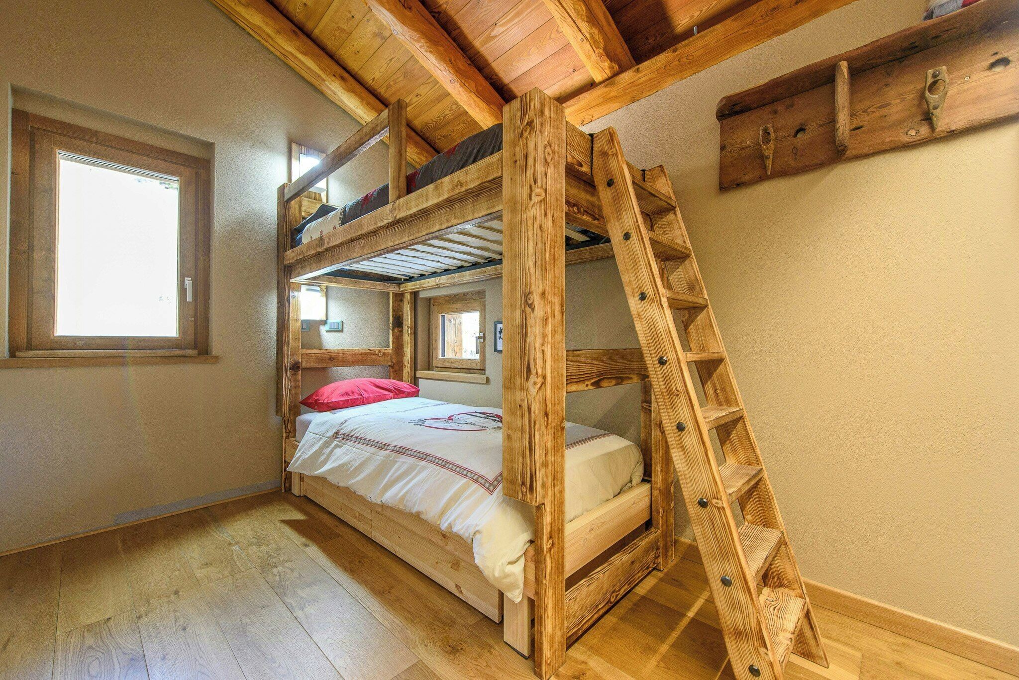 Un lit superposé avec une échelle en bois, une fenêtre et une poutre en bois au plafond.