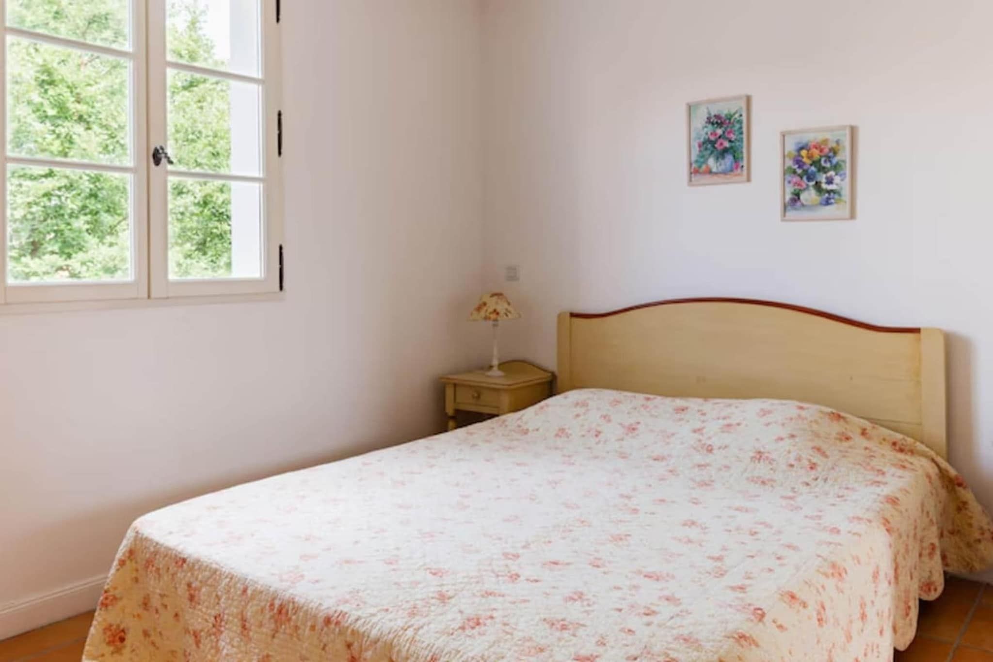 A bedroom with a bed, a nightstand, a window, and two wall-mounted paintings.