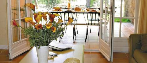 A room with a dining table set for two, a vase with flowers on a coffee table, and a hat.