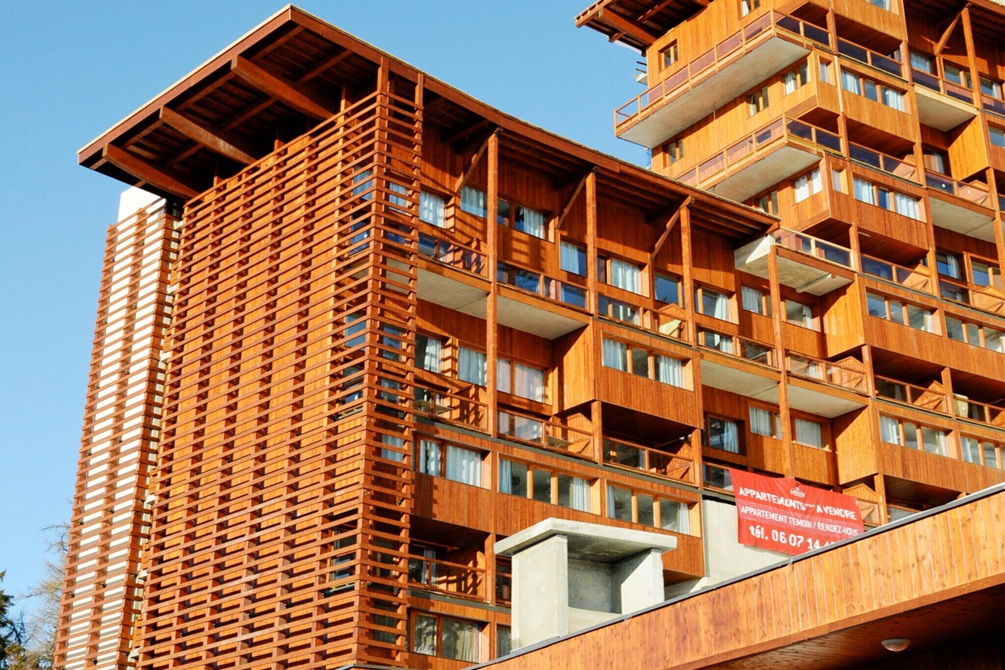 A multi-story building with a wooden facade, balconies, and a sign indicating it is a hotel.
