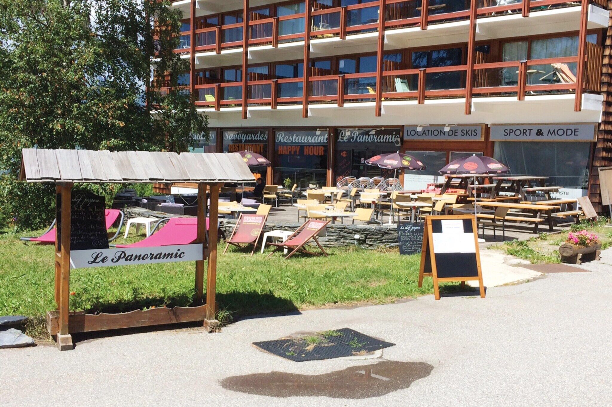 A restaurant named 'Le Panoramique' with outdoor seating and a view of a multi-story building in the background.