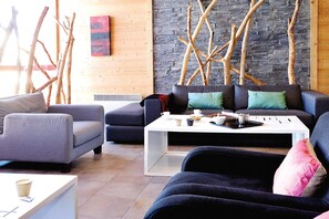 Ein modernes Wohnzimmer mit Steinwand, Holzästen und einer Sofagarnitur.