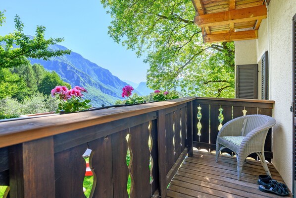 Une terrasse en bois avec une chaise en osier, une rambarde en bois et une vue sur les montagnes.