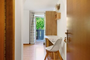 Una habitación con puerta de madera, una silla blanca, una mesa con mantel floral y vistas al exterior con vegetación.