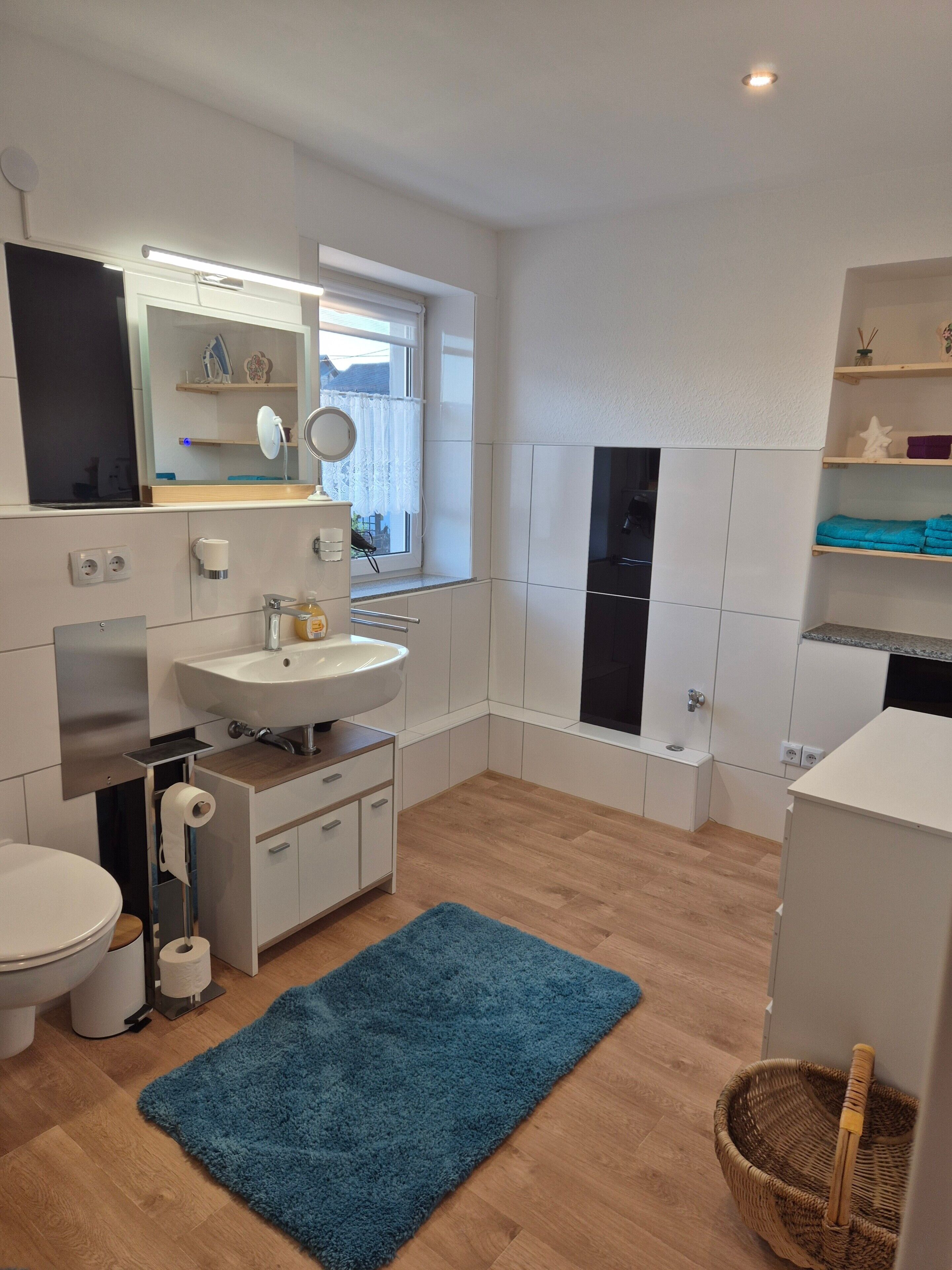 Une salle de bain moderne avec des toilettes, un lavabo, un miroir et un tapis bleu.