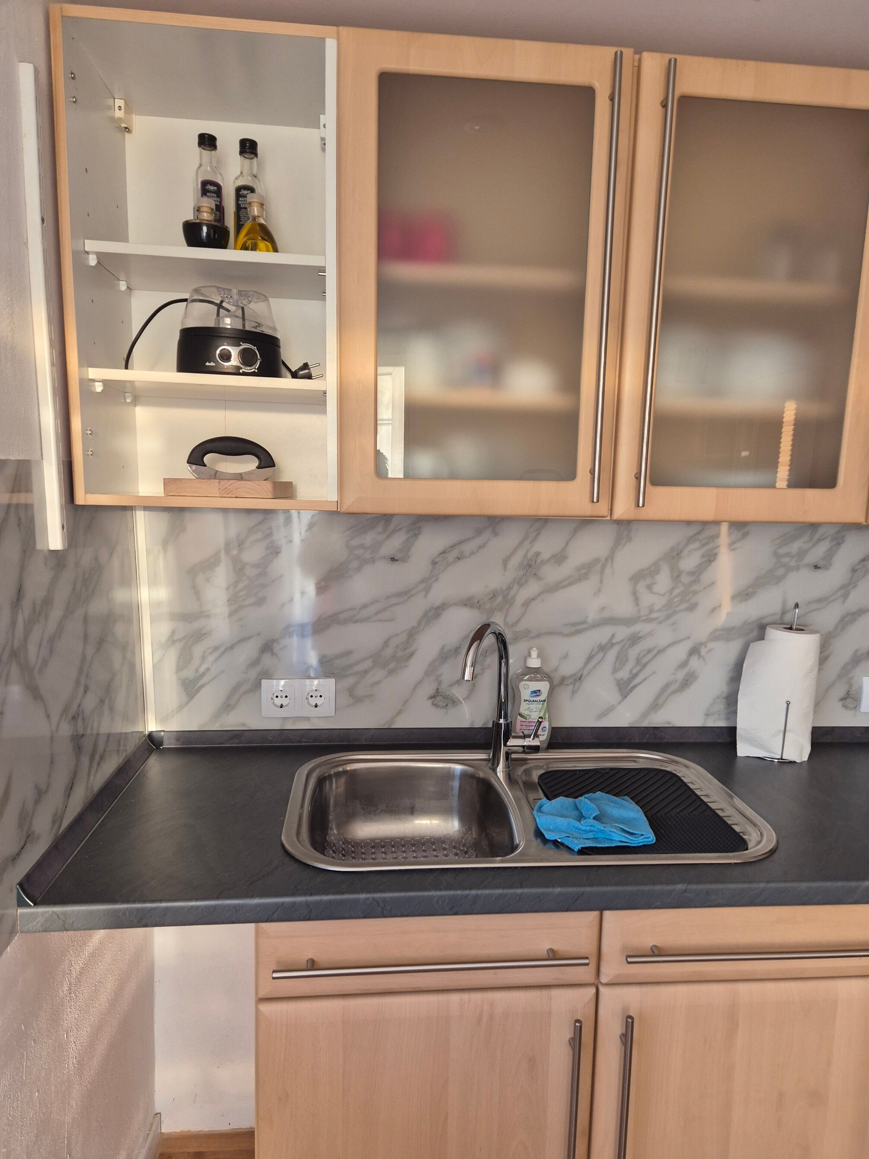 Una cocina con salpicadero de mármol, un lavamanos con dispensador de jabón y armarios de madera.