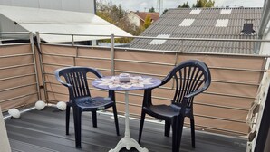 A balcony with a table and chairs, a metal railing, and a view of buildings and power lines.