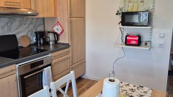 Eine kompakte Küche mit Holzschränken, einem eingebauten Backofen, einer Mikrowelle und einer Kaffeemaschine.