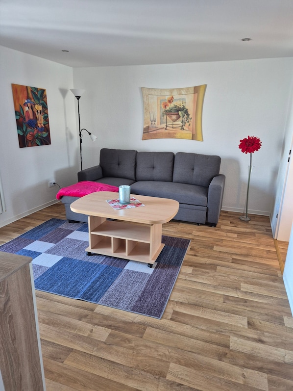 A living room with a grey sofa, a wooden coffee table, a patterned rug, and a painting on the wall.
