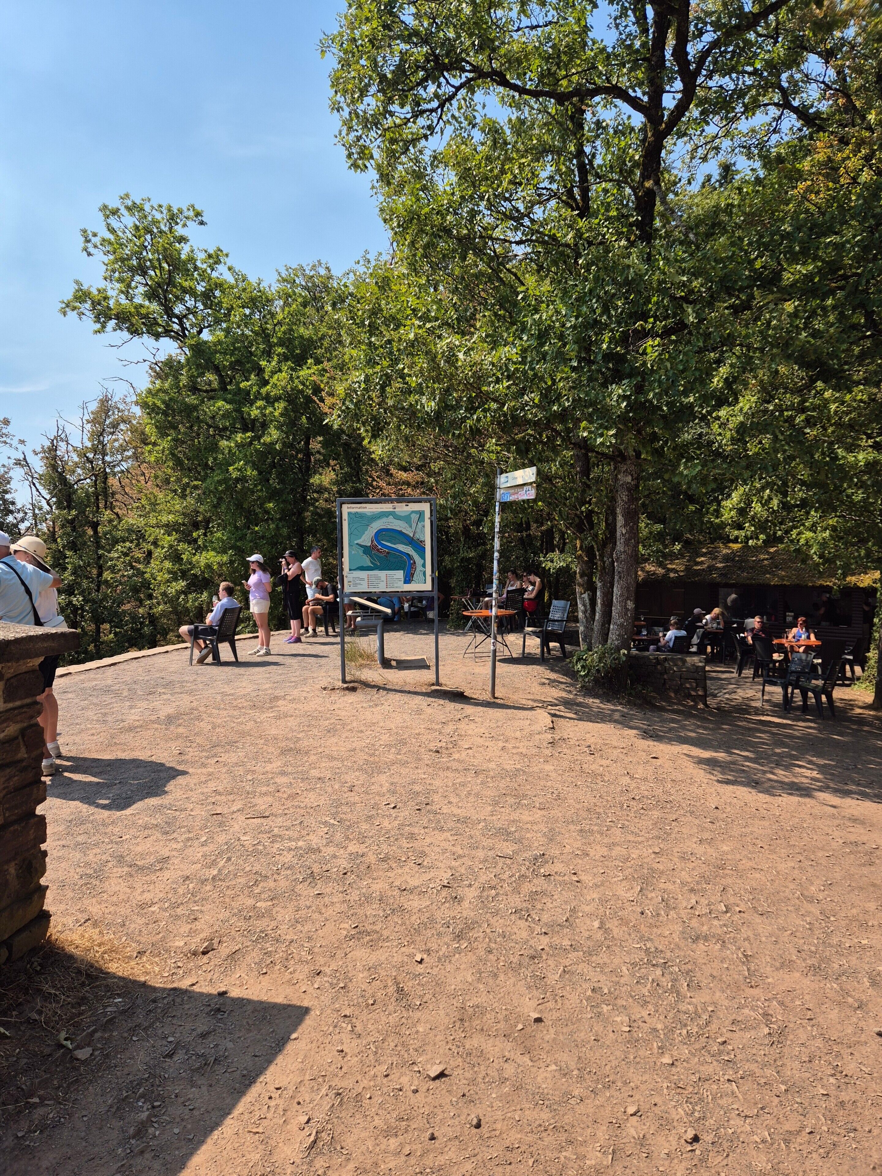 An outdoor area with a dirt ground, a map sign, and people sitting at tables.