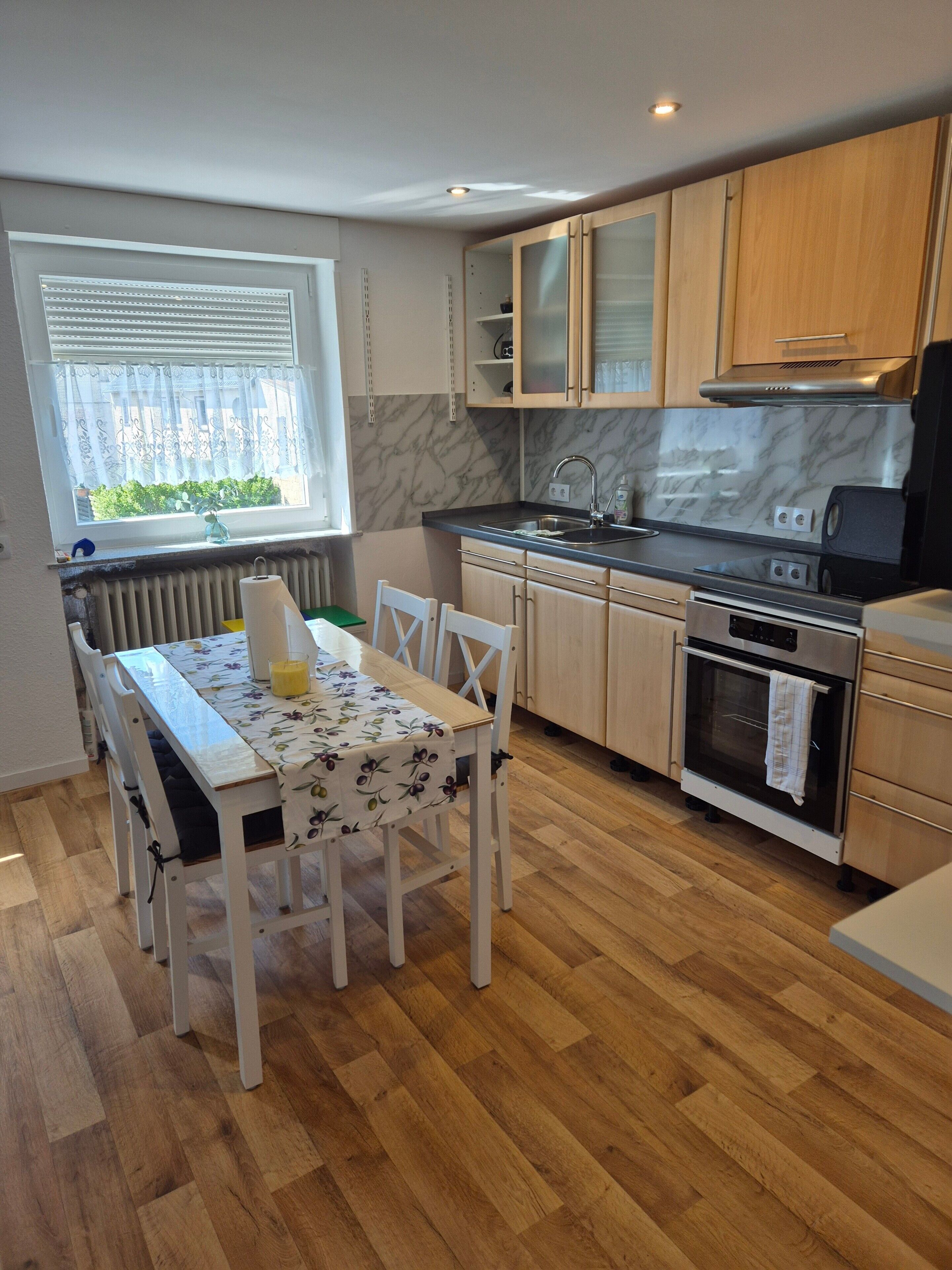 Una cocina compacta con mesa, sillas, horno integrado y ventana con persianas.