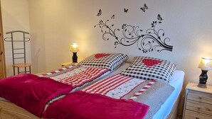 A neatly made bed with patterned bedding, a wooden headboard, a bedside table with a lamp, and a wall decoration with butterflies.