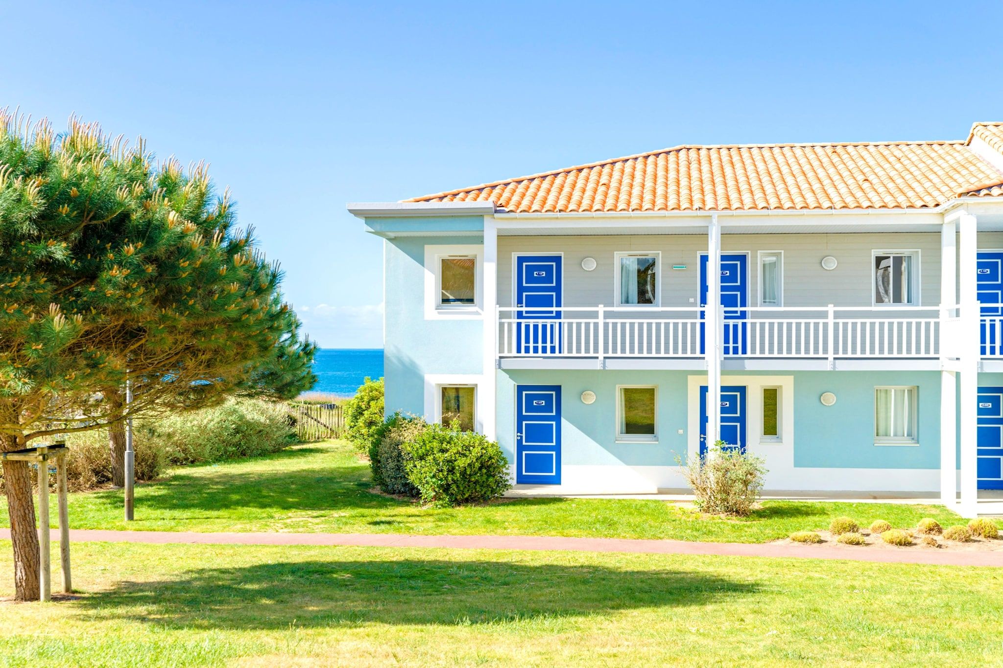 A two-story building with a tiled roof, blue doors, and a balcony.