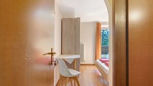 A room with a wooden floor, a white table with a chair, a bed with red bedding, and a window with curtains. - Room 'Rienznerhof Fernblick No. 4' with Mountain View, Shared Terrace & Wi-Fi (Montan an der Weinstraße)