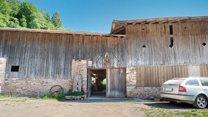 A rustic barn with a dirt driveway, a car parked in front, and a stone wall to the left. - Room 'Rienznerhof Fernblick No. 4' with Mountain View, Shared Terrace & Wi-Fi (Montan an der Weinstraße)
